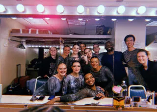 many people gathered in a dresssing room smiling into a mirror